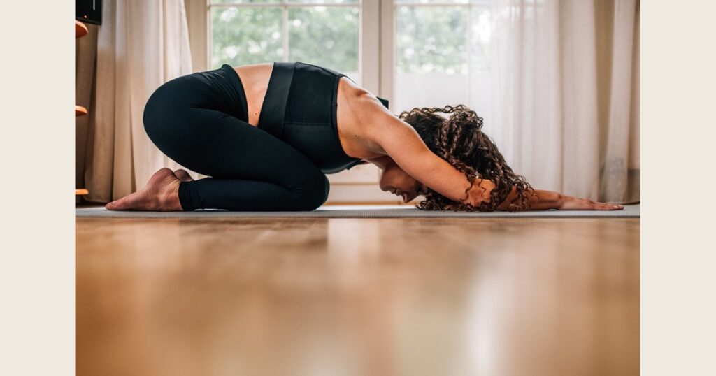 Woman stretching forward in extended puppy pose on a yoga mat.