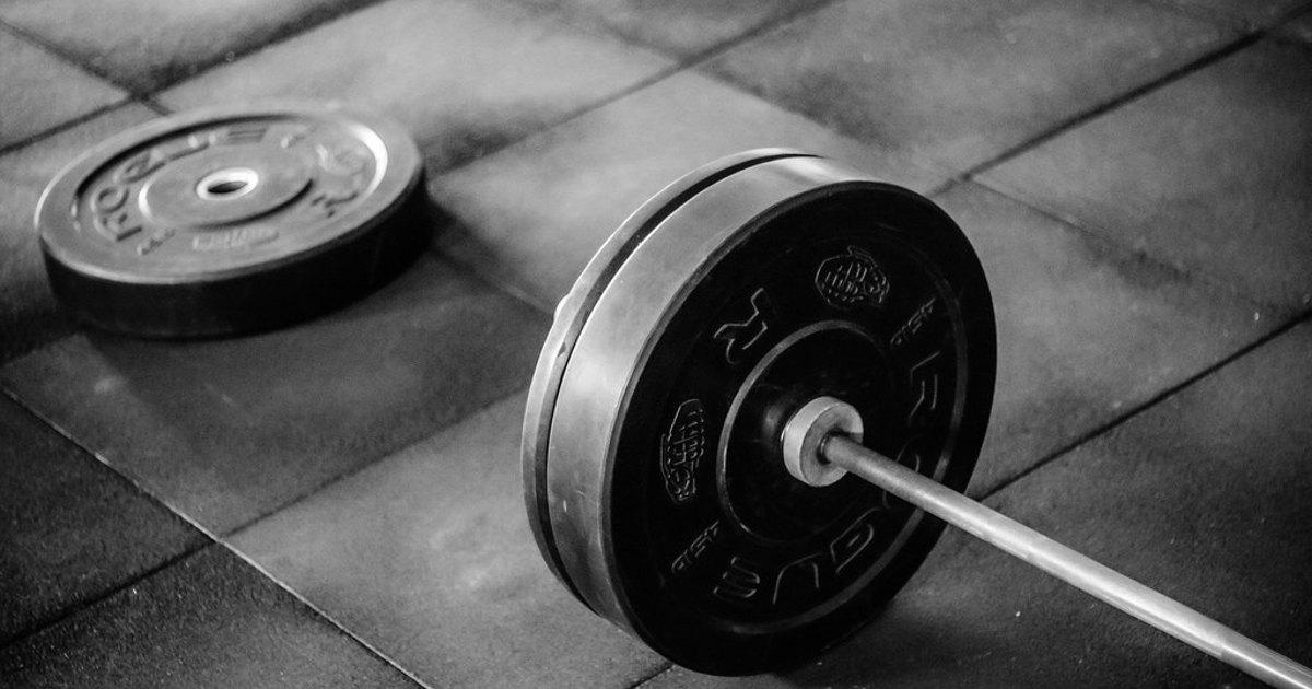 A black adjustable dumbbell resting on a flat surface, with its stacked rectangular weight plates visible around the center handle.